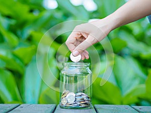 Abstract money saving women hand put coin to glass jar