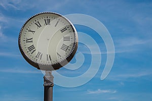 Abstract old fashioned street clock with Roman numerals without arrows on blue sky background. Concept of stopped time