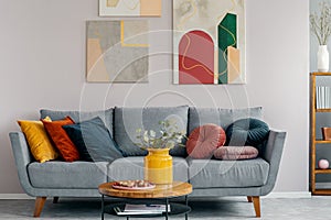 Abstract painting above grey couch with pillows in scandinavian design interior