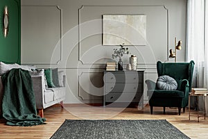 Abstract painting on grey wall o contemporary living room interior with emerald green armchair with round pillow, commode and