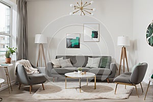 Abstract painting on grey wall o contemporary living room interior with emerald green armchair with round pillow, commode and couc