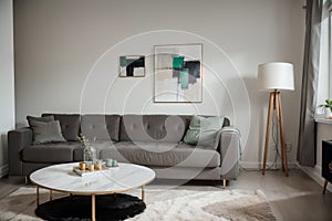 Abstract painting on grey wall o contemporary living room interior with emerald green armchair with round pillow, commode and couc