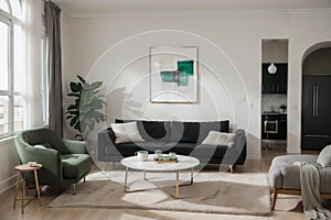 Abstract painting on grey wall o contemporary living room interior with emerald green armchair with round pillow, commode and couc