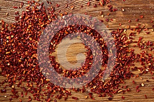 Abstract pattern of dried red hot chilly flakes on rustic wooden background, top view, close-up, macro, selective focus.