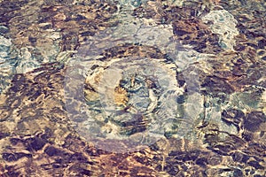 Abstract pattern of pebbles under the surface of the water, texture. Rock bottom background seen through clear water in mountain