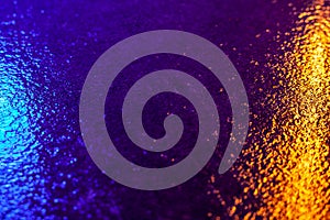 Abstract photo reflection of light on a wet surface. Blue-yellow neon light on a textured wet surface.