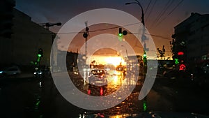 Abstract image through wet car windshield on movng transport and autuomobiles in rain at sunset rays