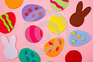 Abstract picture of cut out of felt applications of colourful eggs and white and brown rabbits. Pink background. Flat lay. Easter