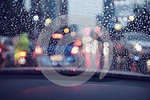 Abstract rain droplets on car windshield with bokeh of traffc at twilight for background