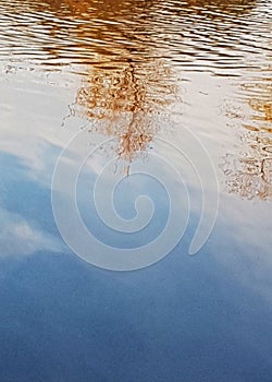 Abstract reflection background yellowed trees, sky with clouds in autumn in the blue water of the river