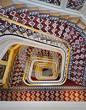 Abstract shape luxurious stairs with red carpet cover and golden handrail. Hypnotic pattern spiral staircase
