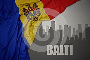 Abstract silhouette of the city with text balti near waving national flag of moldova on a gray background