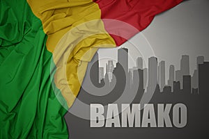 Abstract silhouette of the city with text Bamako near waving colorful national flag of mali on a gray background