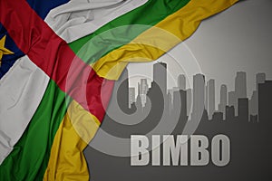 Abstract silhouette of the city with text Bimbo near waving colorful national flag of central african republic on a gray photo