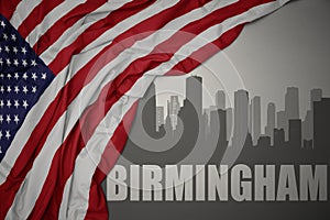 Abstract silhouette of the city with text Birmingham near waving national flag of united states of america on a gray background.