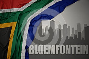 Abstract silhouette of the city with text Bloemfontein near waving colorful national flag of south africa on a gray background