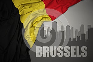 Abstract silhouette of the city with text Brussels near waving national flag of belgium on a gray background