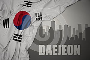 Abstract silhouette of the city with text Daejeon near waving national flag of south korea on a gray background