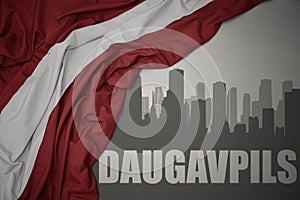 Abstract silhouette of the city with text Daugavpils near waving national flag of latvia on a gray background