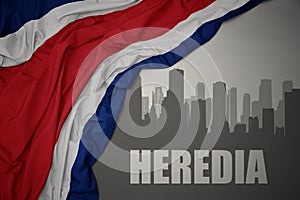 Abstract silhouette of the city with text Heredia near waving national flag of costa rica on a gray background. 3D illustration photo