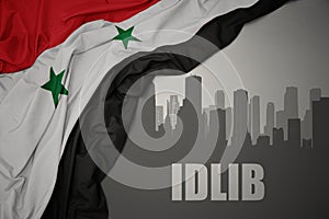 Abstract silhouette of the city with text Idlib near waving national flag of syria on a gray background photo