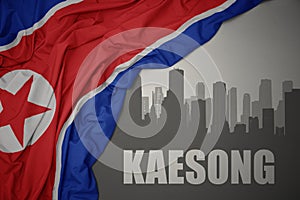 Abstract silhouette of the city with text Kaesong near waving national flag of north korea on a gray background.3D illustration