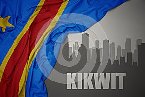 Abstract silhouette of the city with text Kikwit near waving colorful national flag of democratic republic of the congo on a gray