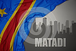 Abstract silhouette of the city with text Matadi near waving colorful national flag of democratic republic of the congo on a gray