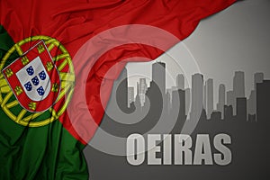 Abstract silhouette of the city with text Oeiras near waving national flag of portugal on a gray background