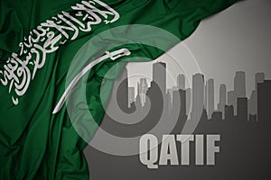 Abstract silhouette of the city with text Qatif near waving national flag of saudi arabia on a gray background photo