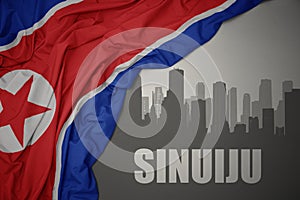Abstract silhouette of the city with text Sinuiju near waving national flag of north korea on a gray background.3D illustration