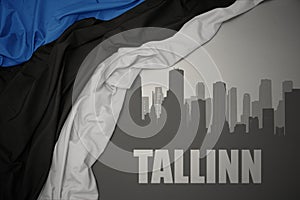 Abstract silhouette of the city with text Tallinn near waving national flag of estonia on a gray background