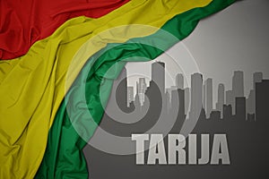 Abstract silhouette of the city with text Tarija near waving national flag of bolivia on a gray background photo