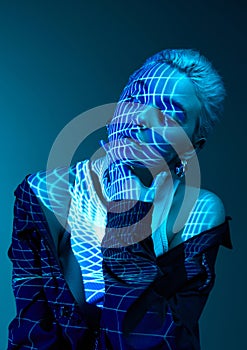 Abstract techno photo. Portrait of young blonde girl with neon stripes on face posing over dark background in blue neon