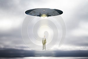 Abstract UFO with light taking businessman on sky background with mock up place. Spaceship and mystery concept