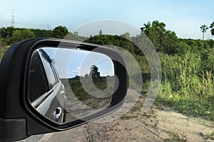 Abstract view of nature beside cars from behind through the mirrors wing of a gray car.