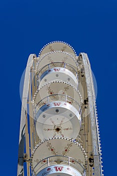 Abstract view from the side of a Ferris wheel with white gondolas at a fair without passengers in the car in front of a blue sky