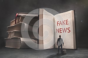 Abstract vision of a businessman standing in front of a huge book with fake news inscription