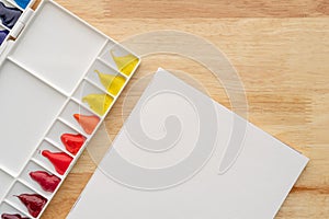 Abstract watercolor paints for background. White palette with white paper on wood
