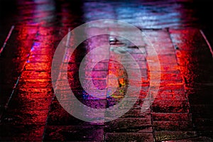 Abstract, wet pavement illuminated at night by colorful lights