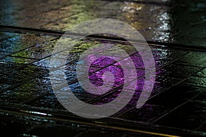 Abstract, wet pavement illuminated at night by colorful lights