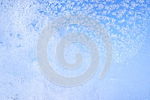 Abstract winter background. Frost on a frozen window against the blue sky.