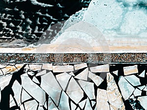 Abstract winter ice background texture of cracked frozen river water surface and floating ice pieces stone pier from above