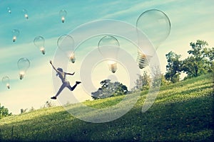 Abstract woman running and jumping for catching light bulb on green grass and flower field