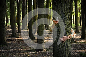 Young woman with Glass of Rose Wine Hugging Tree in Forest