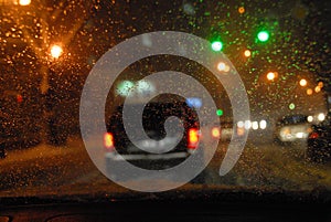 Abstraction. Blurred night urban view with cars, bright traffic lights through wet car windshield in blurred rain drops