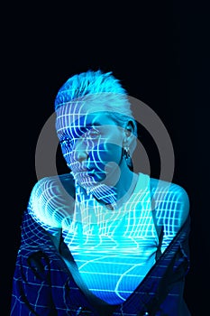 Abstraction and illusion. Portrait of young blonde girl with neon stripes on face posing over dark background in blue