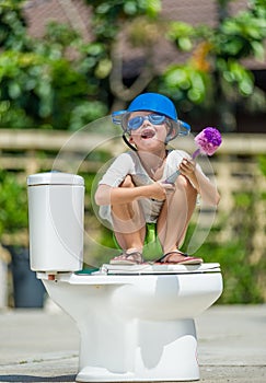 Absurd picture: cute boy in goggles sitting on the toilet, which