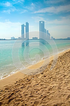 Abu Dhabi skyline with skyscrapers in the background across the ocean & a beautiful beach in the foreground, United Arab