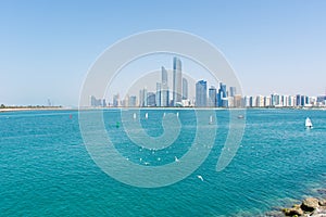 Abu Dhabi, United Arab Emirates skyline with a bright blue sky, sailboats, seagulls and landmark buildings in background. Luxury